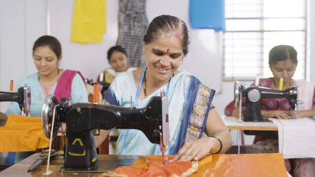 Happy smiling woman showing thumbs up sign by looking camera while working at garments sewing maching - concept of employment, job and successful business
