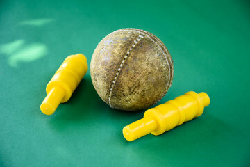 Closeup old cricket sport equipments on green floor, old leather ball and yellow plastic wickets, soft and selective focus, traditional cricket sport lovers around the world concept.