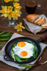 Fried eggs with fried green wild garlic in a cast-iron frying pan. Breakfast with fresh wild garlic. Spring seasonal products concept