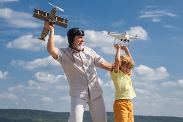 Young grandson and old grandfather with plane and quadcopter drone over blue sky and clouds background. Elderly old relative with child.