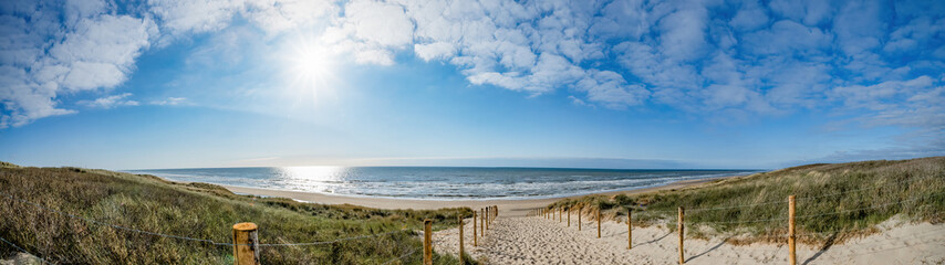 Ein Weg mit vielen Bahnen, begrenzt durch Holzpfähle auf der Sanddüne mit wildem Gras und Strand in Noordwijk an der Nordsee in Holland Niederlande - Panorama Meereslandschaft mit blauem Himmel und Wolken