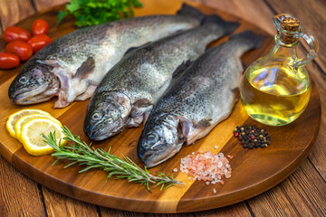 Three raw trout with spices and olive oil on a wooden board.