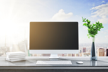 Close up of modern designer desktop with books, blank computer screen, decorative plant, supplies and bright city and sky view background. Mock up, 3D Rendering.
