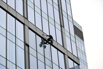 Climber wash windows and glass facade of the tower building. Window cleaner on the skyscraper wall