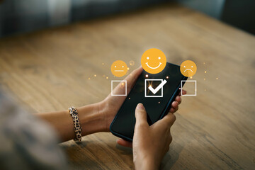 concept of customer service evaluation and satisfaction, a young woman Using mobile phone pressing a smiley face emoticon on the smartphone and displayed shown on a virtual screen.