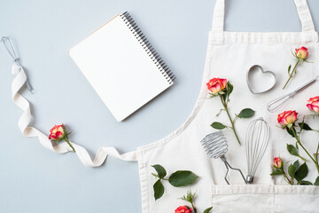 Blank recipe cooking book, baking accessories with apron with flowers roses on a gray background, flat lay, top view. Festive baking recipes concept