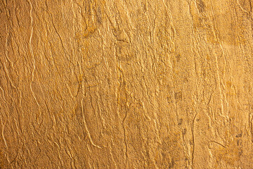 Golden wall with abstract spots as a background. Beautiful golden texture with patterns, decorative plaster. Modern bright wall painting in trendy shades, unusual spotted yellow and gold surface.