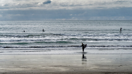 Fototapeta na wymiar Surfers and stand up paddle boarders at Sumner Beach, Aotearoa / New Zealand.
