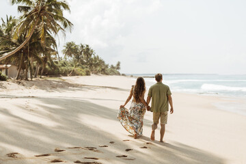 Couple in love walking along the beach under palm trees