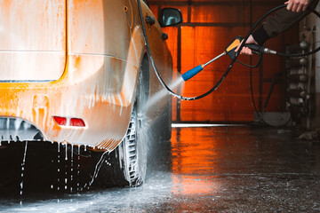 Washing a yellow car at a contactless self-service car wash. Washing a sedan car with foam and high-pressure water. - obrazy, fototapety, plakaty