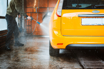 Washing a yellow car at a contactless self-service car wash. Washing a sedan car with foam and...