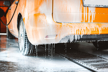 Washing a yellow car at a contactless self-service car wash. Washing a sedan car with foam and...