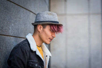 Side portrait of handsome trendy hispanic young boy with denim and hat looking in front of you. Urban wall in background. Concept of modern teenager with different style and colorful hair