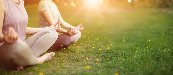 Two women sitting in active wear in lotus position in nature.