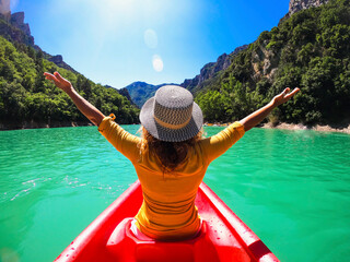Back view of a woman with hat outstretching arms for happiness sitting on a red canoe kayak in a...