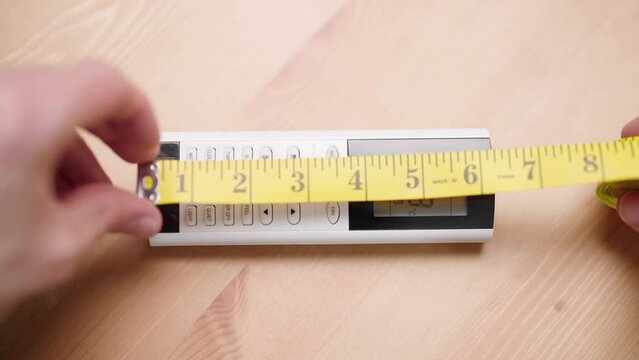 Person with measuring tape measure size of 6 inch remote controller on table 4K