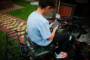 Boy in four-wheller ATV quad bike with mobile phone.