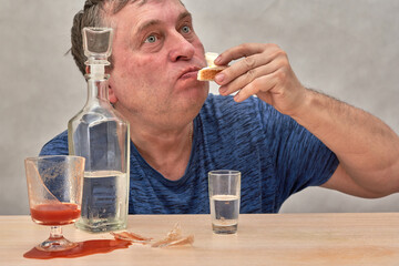 The drunkard brought a snack to his mouth while eating a glass of vodka - 502724988