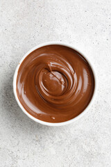 Chocolate sauce in a white saucer on grey background. Curl of Liquid chocolate. Top view.