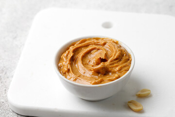Peanut butter in a white saucer on white board. Curl of Peanut butter with peanut. Copy space