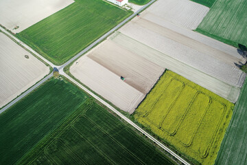 drone aerial view of some fields of rapeseed and cereal crops and two tractors plowing the soil.