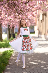 A beautiful girl in a Ukrainian vyshyvanka. Ballerina in cherry blossoms. Ballet on the street. Ukrainian girl