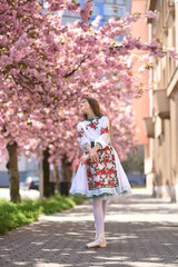 Fototapeta premium A beautiful girl in a Ukrainian vyshyvanka. Ballerina in cherry blossoms. Ballet on the street. Ukrainian girl 
