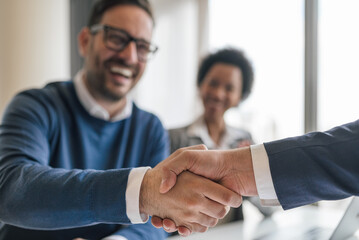 Fototapeta na wymiar Happy businessman shaking hands with partner on successful deal at office