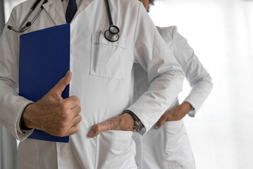 Confident doctors with hands in pockets against white background