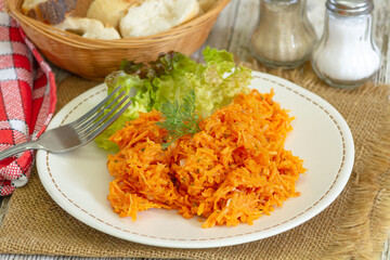 grated carrot in a plate with salad on a table
