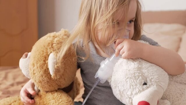 little girl three-year-old uses nebulizer, inhaler, breathes medicine. Treatment of asthma, bronchitis, lung diseases. Home room, indoors. hugs toys