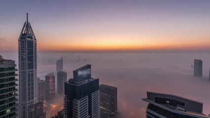 Rare early morning winter fog above the Dubai Marina skyline and skyscrapers lighted by street lights aerial night to day timelapse.