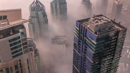 Naklejka na ściany i meble Rare early morning winter fog above the Dubai Marina skyline and skyscrapers rooftops aerial timelapse.