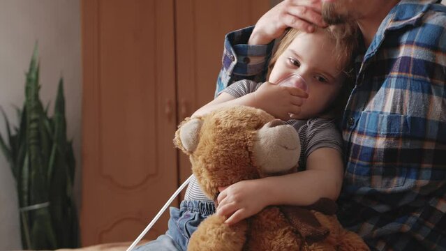 child suffers, lung cancer, sad atmosphere, home room, indoors. Dad comforts his daughter, helps, pats on head, loves. child breathes medications and oxygen with nebulizer, inhaler. hugs toy