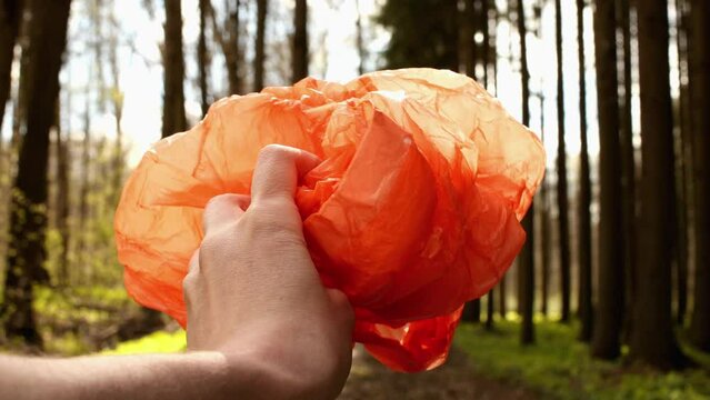 Orange plastic bag in young man left hand in the green forest. Pavel, my hand and plastic bag. Date of shooting day 4 May 2022 year, MSK time. This video was filmed in Russia.