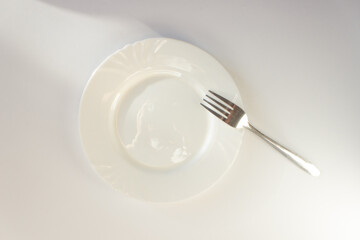 Empty dinner plate with silver fork isolated on white background. Top view. Diet and fasting day concept.