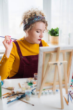 Beautiful woman artist paints on canvas at home