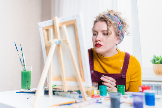 Beautiful woman artist paints on canvas at home