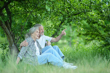 Nice mature couple sitting on green grass in summer park