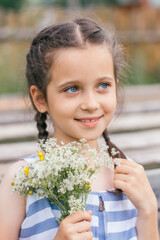 Portrait of a cute dark-haired blue-eyed girl with a bouquet of wildflowers.Childhood, summer, rural simple life, positive vibes.