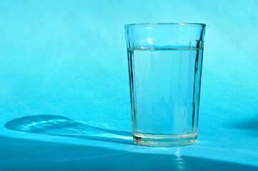Glass with clean fresh drinking water on a blue background. Daylight, sun and shadows. Front view with copy space