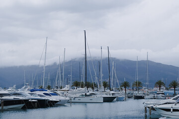 Fototapeta na wymiar yachts in marina on a cloudy sky day over mountains landscape. luxury transport in a port. sailing boats in calm adriatic sea, Porto Montenegro