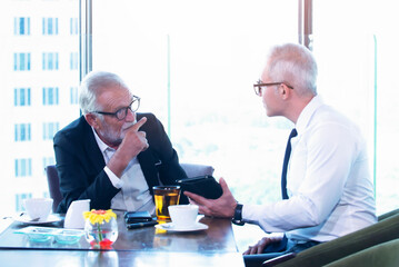 Senior businessman discuss information with a younger colleague in a modern business lounge.