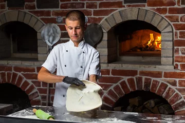 Tuinposter Pizza chef tossing pizza dough in the air in a traditional pizzeria kitchen © bondvit