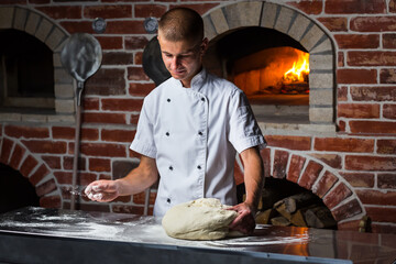 Italian pizza chef sprinkle flour on dough on a floured surface in a traditional pizzeria kitchen