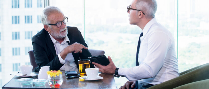 Senior businessman discuss information with a younger colleague in a modern business lounge.
