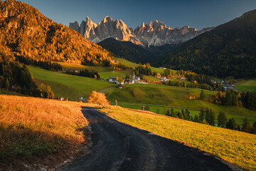 Autumn sunset in Val di Funes in the Italian Dolomites. Fall colors create beautiful contrasts with the blue sky.