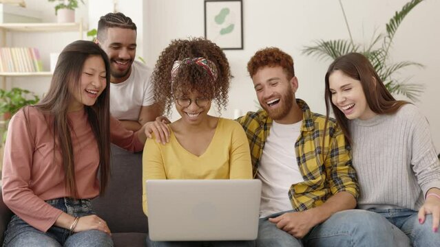 Young group of multiracial people using laptop computer together on sofa - Millennial diverse student friends having fun watching videos or movies on streaming platform