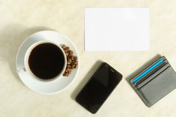 Fototapeta na wymiar A cup of coffee with coffee beans, mobile phone, bank cards and empty blank on the table.