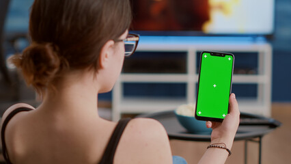 Closeup of young woman holding vertical smartphone with green screen watching social media content...